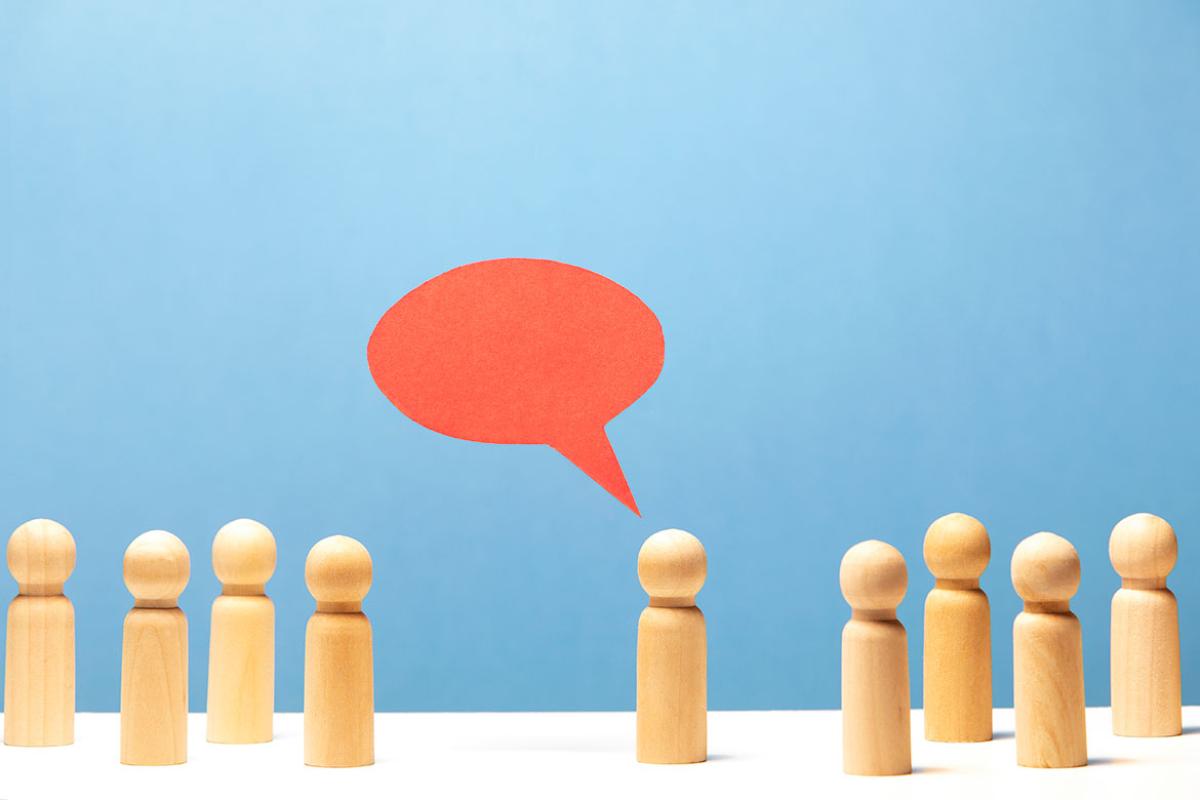 Red speech bubble in mid air over wooden figurine surrounded by 8 other figurines